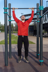 Man in red shirt doing pull-ups at an outdoor gym. The blue sky suggests a sunny day for a workout and active lifestyle