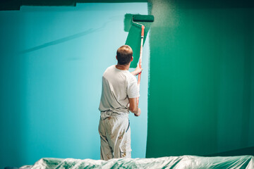 Professional painter applying green paint on wall with roller