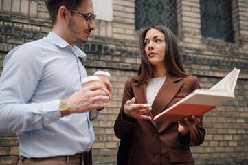 Business colleagues discussing work while holding coffee and book outdoors