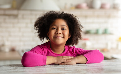 Closeup Portrait Of Cute Curly Black Girl Sitting At Table In Kitchen, Positive African American...