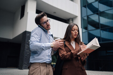 Businesspeople working outside office building using mobile phone and taking notes