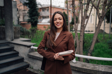 Smiling businesswoman holding books is walking in the city park