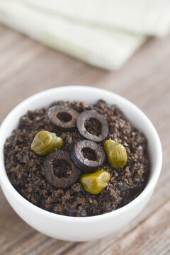 Homemade french black olive tapenade spread garnished with olive slices and capers, served in a small bowl (Selective Focus, Focus one third into the image) 