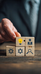 Wooden cubes with business icons arranged in a grid with a hand placing one strategy concept