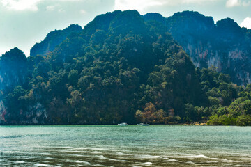 Lush green island with limestone cliffs in turquoise waters, under a clear blue sky, Krabi, Thailand.