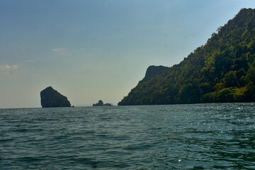 Lush green islands rise from the calm sea under a bright sky near the coast of Krabi, Thailand. 