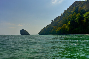 Lush green islands rise from the calm sea under a bright sky near the coast of Krabi, Thailand. 