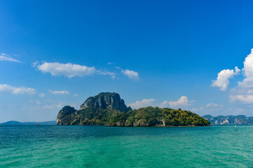Fototapeta premium Lush green island with limestone cliffs in turquoise waters, under a clear blue sky, Krabi, Thailand.
