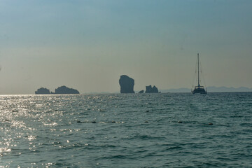 Ocean view with distant islands and a sailboat, bathed in sunlight in Andaman sea.