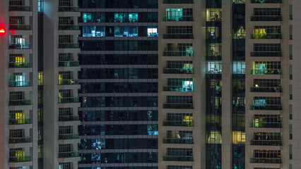 Rows of glowing windows with people in apartment building at night.