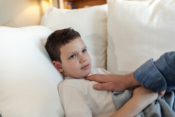 Parent, bed and care with sick child for virus, illness or infection from cold or flu at home. Father with little boy, kid or son in rest, fatigue or weakness with love or support in bedroom at house.