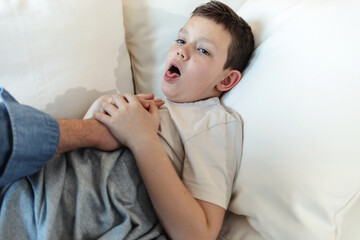 Sick, boy and parent in home, coughing and hand on chest of child, bedroom and kid with virus of flu. House, fever and youth in pain, bed and support with love of father, childcare and monitoring,