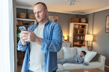Father on a phone call about his sick son, looking for medical advice. Ill and unhappy boy with flu and fever while his dad is talking about online healthcare insurance at home.