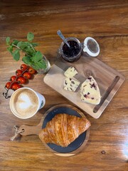 French breakfast featuring golden croissant nestled on rustic wooden board, paired with cranberry cheese, blueberry jam, artisan cappuccino, cherry tomatoes, mint, true French breakfast indulgence.