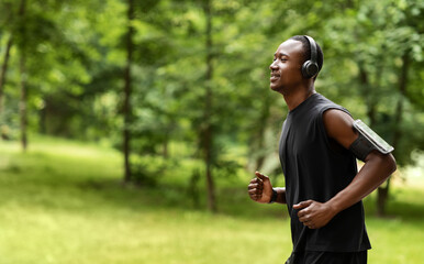 Side view of african guy jogger training at city park, running towards copy space