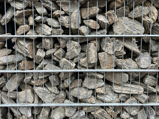 Fragment of a fence made of split stones placed in a metal mesh enclosure as a background