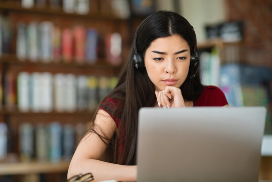 Webinar. Focused asian girl studying online with laptop and headset at cafe, watching educational videos, copy space