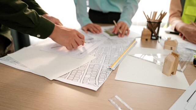 Smart architect and safety engineer discussion about building blueprint on table with architectural document, measurement tools and wooden block scatter around at modern office. Closeup. Delineation.