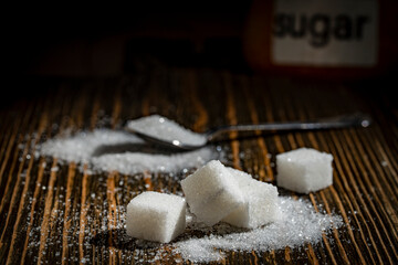 White cube sugar and granulated sugar on wooden background, closeup. The concept of unhealthy eating, obesity, heart disease, diabetes
