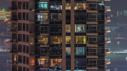 Rows of glowing windows with people in apartment building at night.