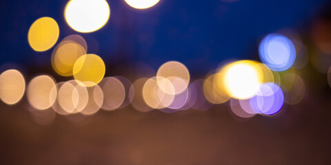 Blurred abstract background with colorful bokeh lights at night. Circular defocused city lights in warm yellow, orange, and blue tones. Ideal for use in design projects, website backgrounds