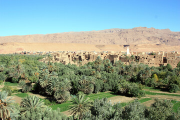 Aït Benhaddou, a traditional desert village in Morocco, featuring earthen clay houses and palm trees set against a rocky and arid backdrop. 