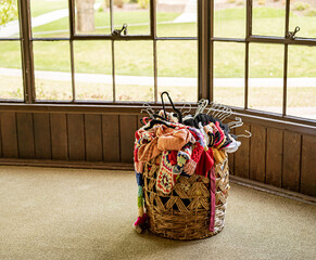Large wicker basket filled with colorful clothing on hangers in front of windows