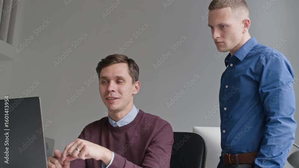 Wall mural positive male project manager pointing at computer screen discussing job tasks with colleague while 