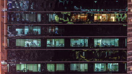 Office skyscraper exterior during late evening with interior lights on and people working inside...
