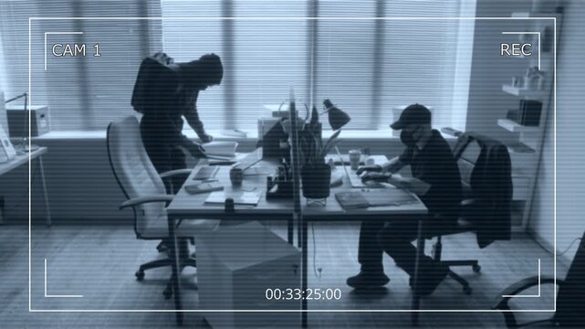 Security camera footage of male criminal hacking into corporate laptop while accomplice searching for confidential data in documents during industrial espionage in office room