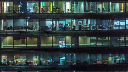 Working evening in glass office building with numerous offices with glass walls and windows...