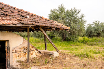 Old rural storage building with a tiled roof and earthen walls, located in a grassy field in Turkey. Abandoned and weathered, possibly used as an icehouse or food cellar in the past.