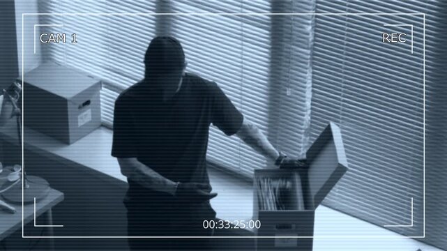 Security camera footage of male criminal hacking into corporate computer in office while partner rummaging through documents in box searching for confidential data during industrial espionage