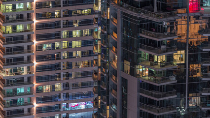 Rows of glowing windows with people in apartment building at night.