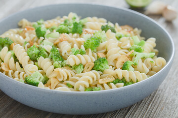 Fusilli or rotini pasta with broccoli, roasted garlic slices, herbs and olive oil, served in blue bowl (Selective Focus, Focus one third into the dish)