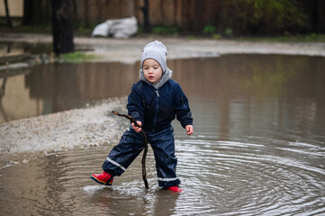 Happy Child Jumping in Rainy Puddle Outdoor Fun in Waterproof Clothes