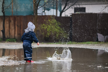 Happy Child Jumping in Rainy Puddle Outdoor Fun in Waterproof Clothes