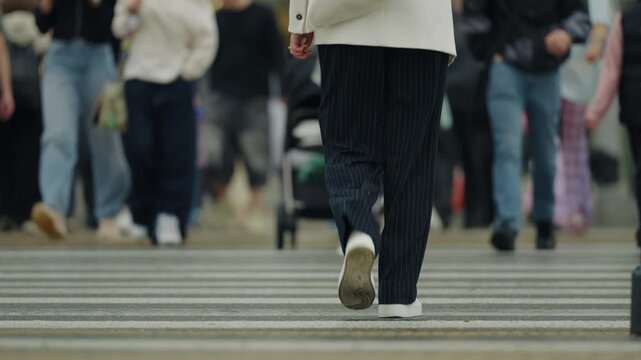 Out of focus bokeh low angle shot of people walking across a busy city crosswalk on a rainy day in summer or autumn. Urban street scene background with wet pavement and foot traffic