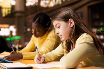Multiethnic scholars doing their homework at a library desk after classes, engrossed in literature...
