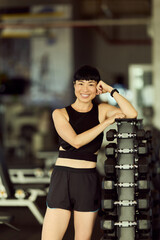 Woman Smiling Confidently in a Fitness Gym by a Dumbbell Rack
