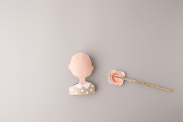Art project step showing doll head painted with peach color on gray surface, great for DIY tutorials, early education tools, craft supply branding, children content, creative teaching,