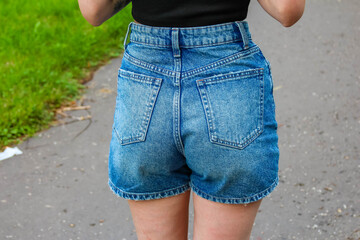 Young woman wearing casual denim shorts standing on grass showing summer fashion and lifestyle
