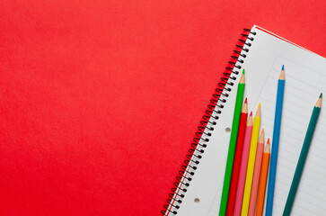 A notebook and some colorful pencils on red background and copy space. 