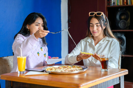 Two latin women enjoying pizza and drinks at restaurant