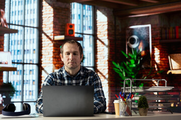 Man seated at home office desk using laptop, checking emails displayed on screen, reading messages...