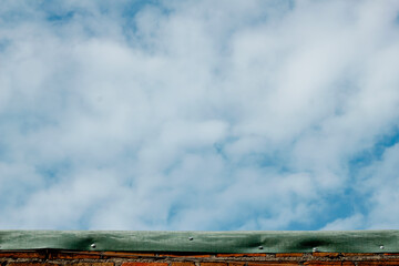 beautiful clear sky with white clouds, captured above a weathered brick wall with a green material atop. © Restu