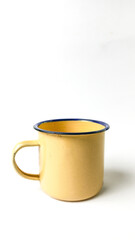 simple still life featuring a yellow enamel mug with a blue rim, set against a clean white background.