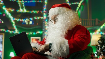 Man dressed as Santa Claus responding to kids requesting gifts, typing on laptop. Person...