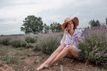 Young sexy beautiful woman enjoying the scent of flowers, nature and relaxation while sitting in a lavender field. Recovery. Wellness. Peace of mind.
