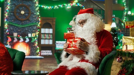 Amazed Santa Claus surprised to find gift box for him in cozy Christmas decorated room. Elderly man...